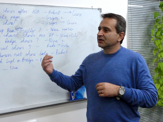 A man with a blue sweater in front of a whiteboard.
