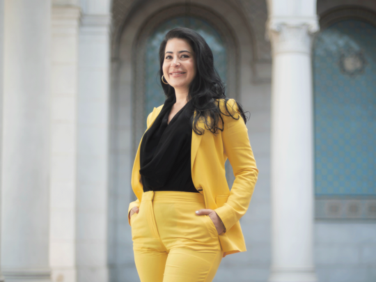 A woman in a yellow suit stands in front of  the City Hall, the civic center of Los Angeles, CA